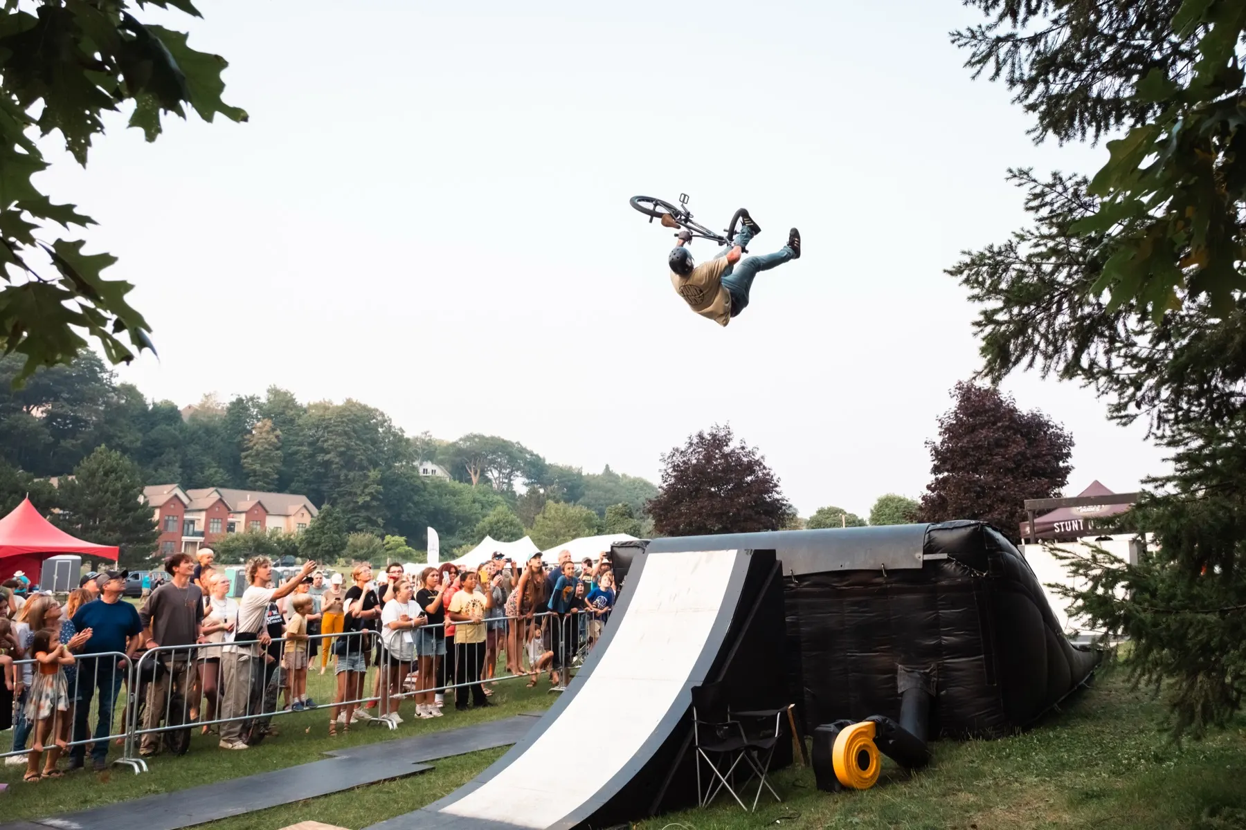 StuntDudes rider mid-backflip over the ramp with hills rising behind the crowd
