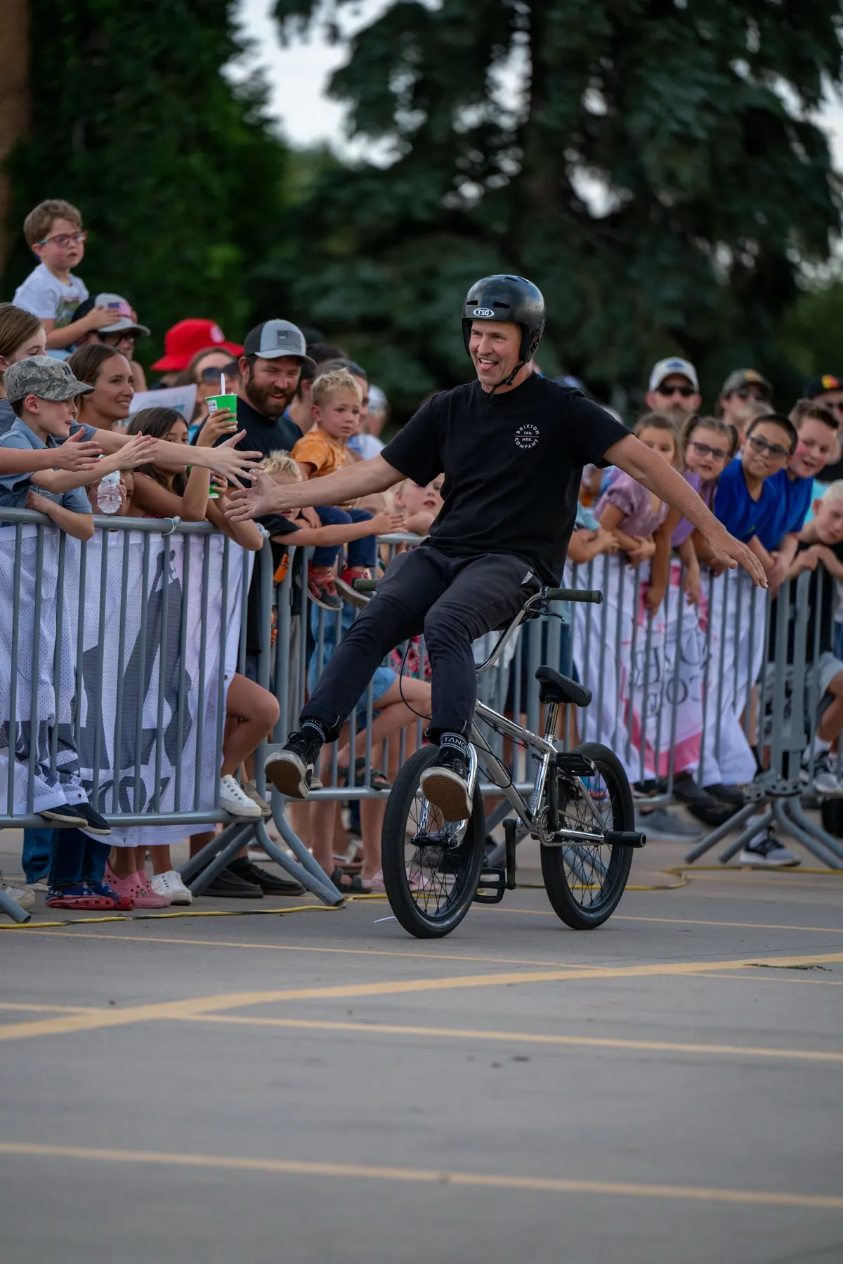 StuntDudes rider on the back wheel at a barrier packed with reaching kids