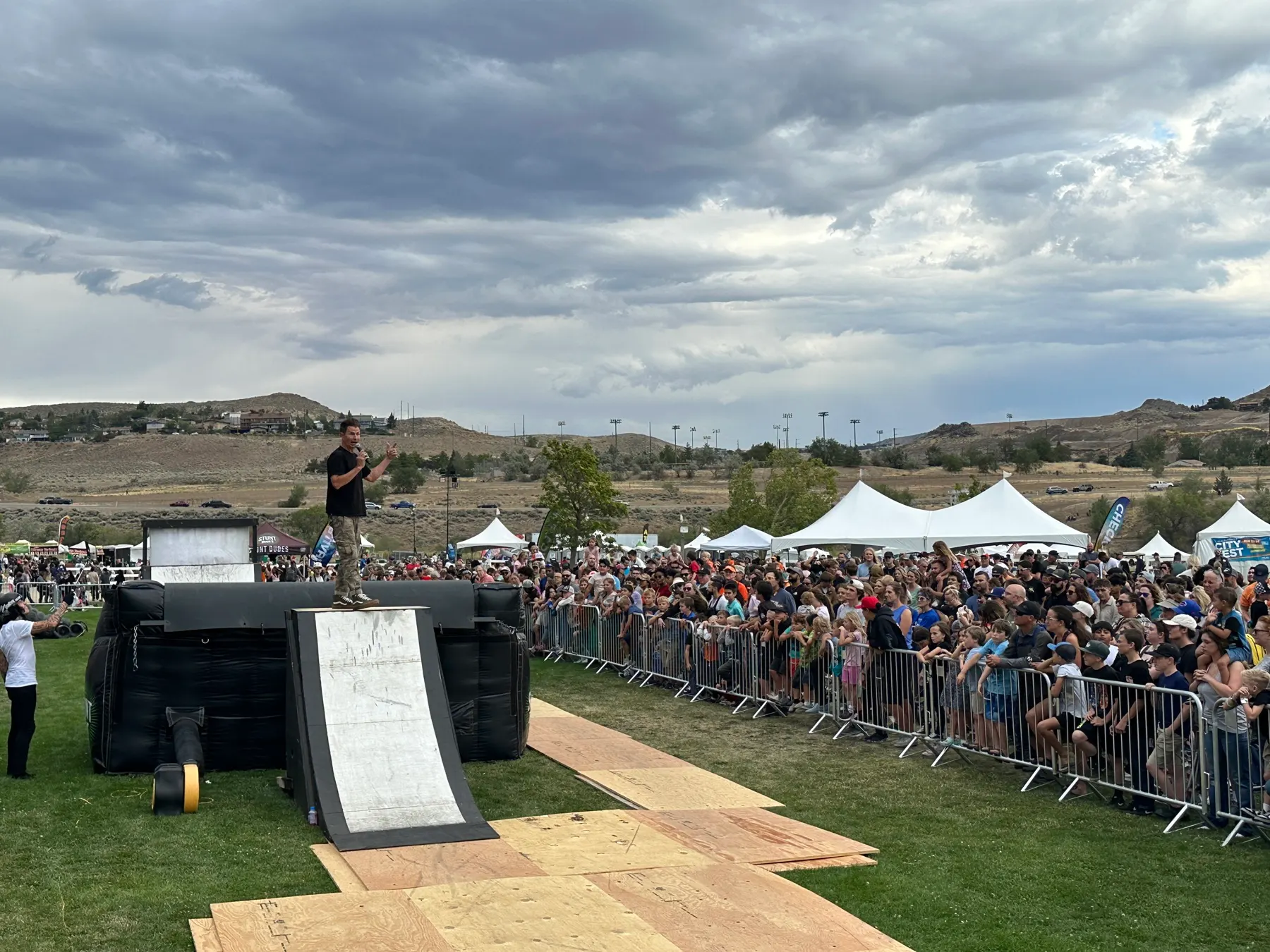 StuntDudes ramp on a festival stage with tents and hills behind the crowd