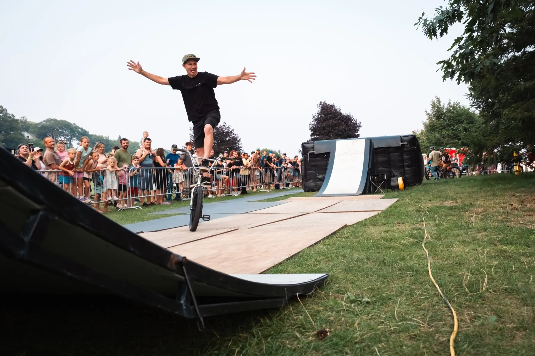 StuntDudes rider standing tall on the bike atop the ramp, arms out to the crowd